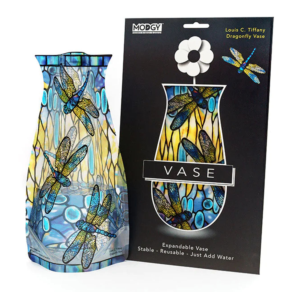 A blue and yellow Louis Comfort Tiffany Dragonfly Expandable Vase with a dragonfly design stands beside its packaging, which has a matching dragonfly motif, the product name, and a white flower illustration.