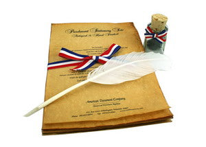 The Parchment Stationery Set includes hand-finished parchment paper tied with a red, white, and blue ribbon, a quill pen, and a small glass ink bottle with cork, all beautifully arranged on a white surface.