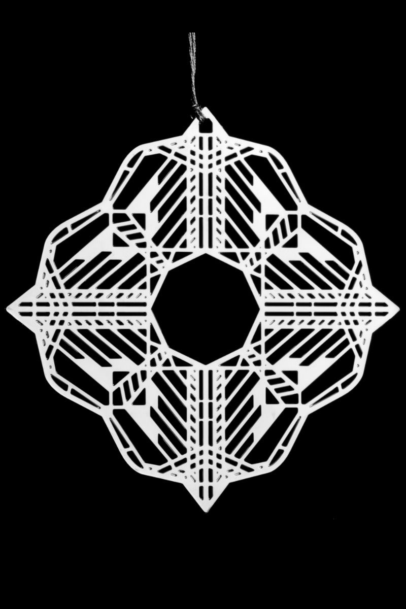 The Frank Lloyd Wright Dana Butterfly 2D Ornament, a white geometric paper snowflake with an intricate symmetrical pattern, hangs by a string against a solid black background, inspired by the Art Glass of Springfield’s Dana-Thomas House.