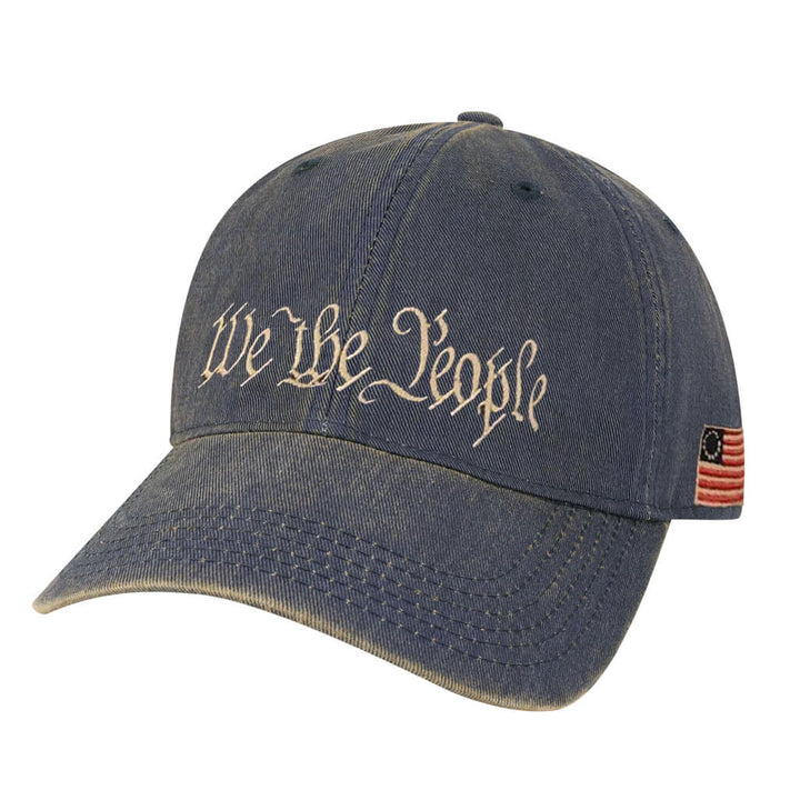 The We the People Cap is a blue denim hat with "We The People" in white script on the front and an American flag patch on the side—ideal for trips to historic sites or expressing your patriotic spirit.