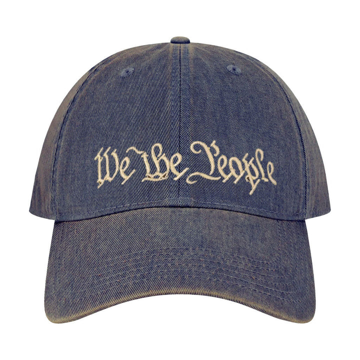 The We the People Cap is a blue denim hat with cream embroidered text on the front, inspired by the Constitution for a stylish tribute to American heritage.