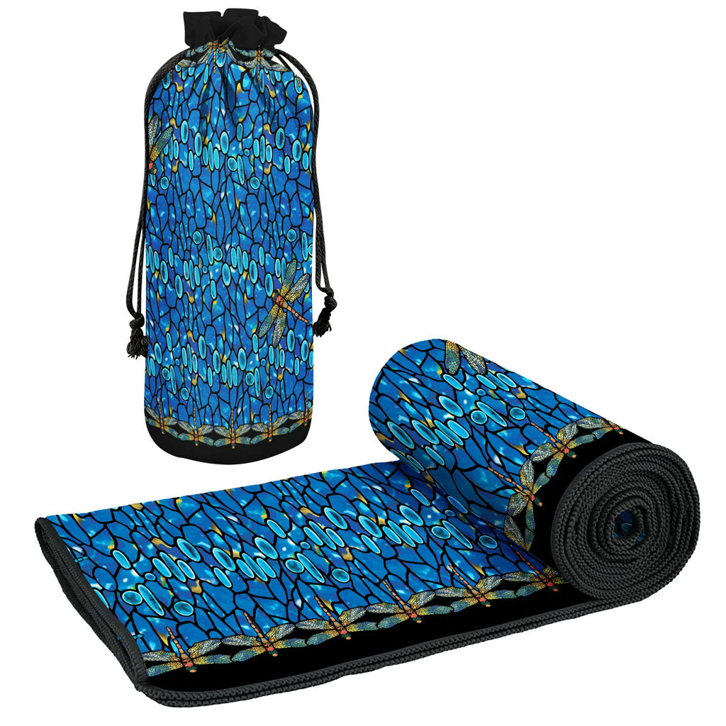 A rolled Louis Comfort Tiffany Dragonfly Beach Towel with a bold blue, black, and gold geometric pattern is shown next to a matching upright drawstring carrying bag.