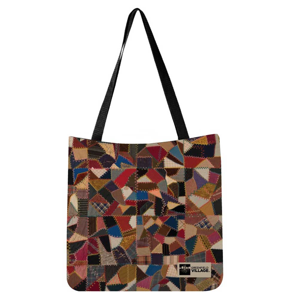 The Quilt Pattern Tote features black handles and a vibrant patchwork design in red, brown, blue, and beige. Inspired by Henry Ford Museum designs, it includes a small rectangular label sewn near the bottom corner.