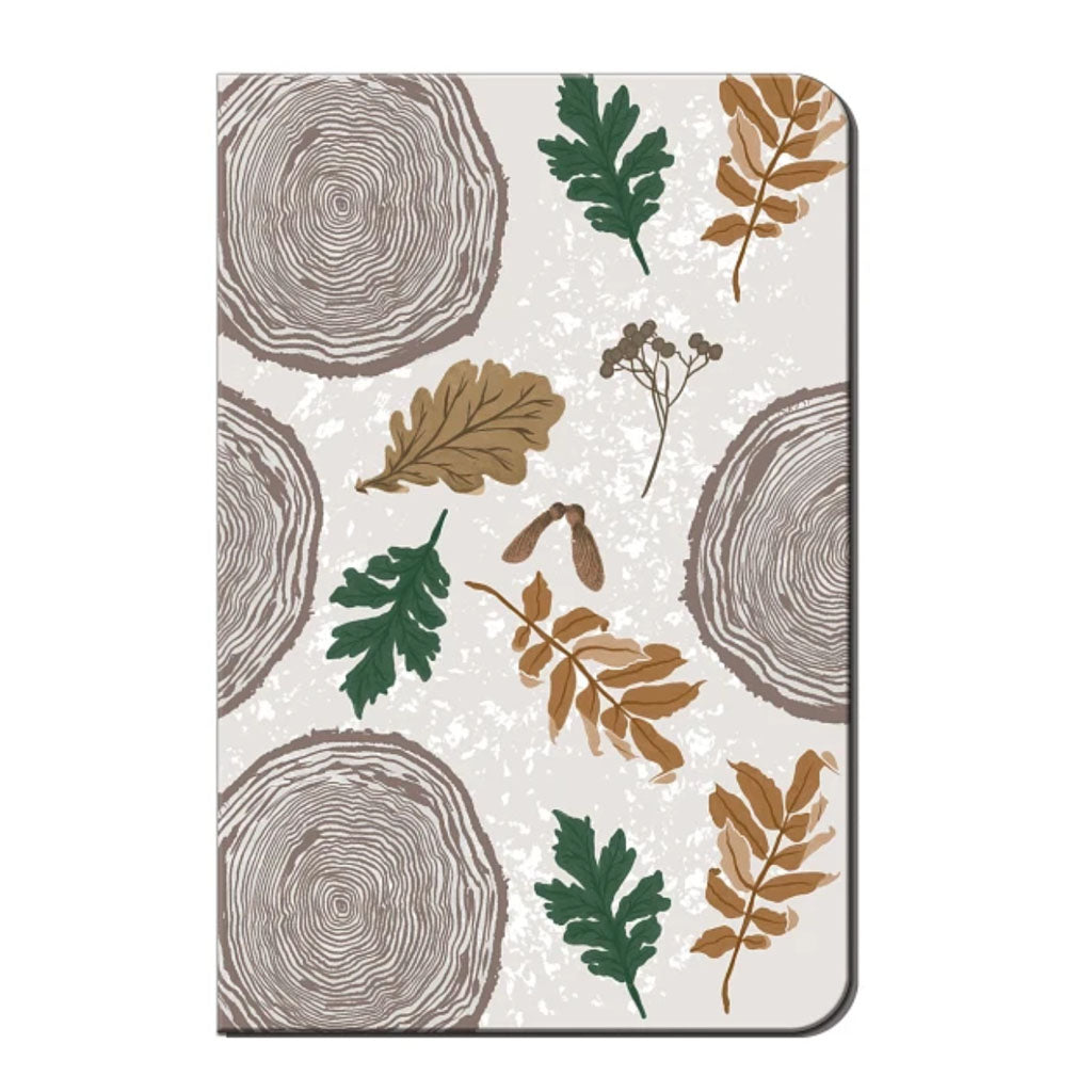 The Wood Tree Journal features a pattern of tree rings, green and brown leaves, branches, and seed pods on a light beige background—ideal as a softcover journal for daily reflections.