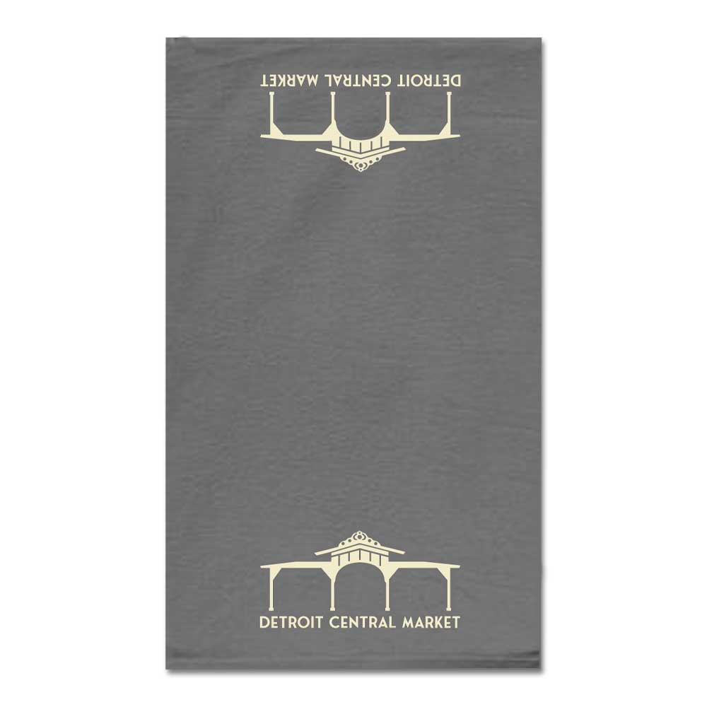 The Detroit Central Market Tea Towel is gray with white DETROIT CENTRAL MARKET text and a market building logo at both ends—one upside down—and is inspired by Greenfield Village.