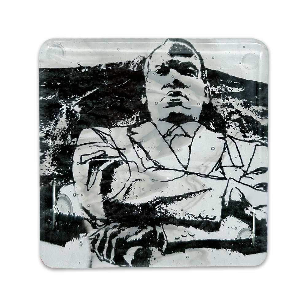 The Martin Luther King Jr. Coaster features a black-and-white illustration of a person in a suit with arms crossed on a textured, abstract background, printed on a glass-like square surface with visible small bubbles.