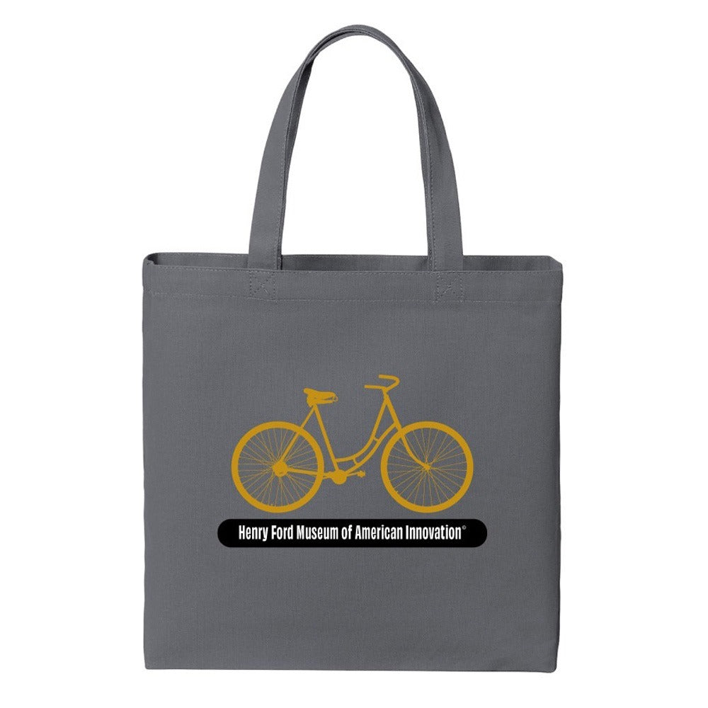 The Henry Ford® Bicycle Tote is a gray canvas bag with a yellow vintage bicycle graphic and "Henry Ford Museum of American Innovation" printed below the bike.