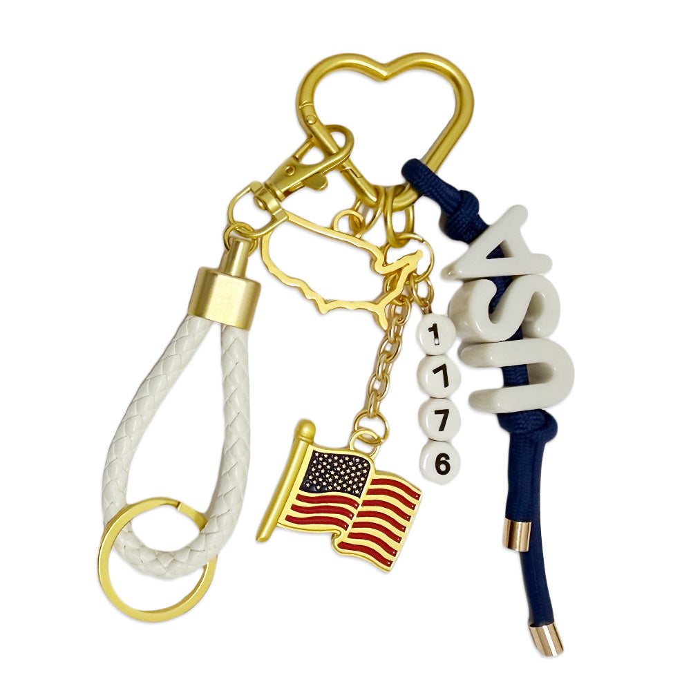 The USA Carabiner Bag Clip features a gold heart carabiner, a white braided loop, a gold U.S. outline, an American flag charm, and “USA” and “1776” beads on navy cord—a patriotic accessory for any backpack.