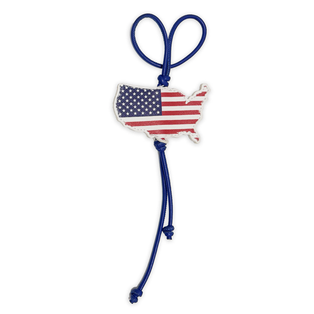 A blue cord loops through the PU Flag Bag Clip, shaped like the US and decorated with stars and stripes. Two knotted ends hang below—perfect as a patriotic travel accessory or backpack charm.