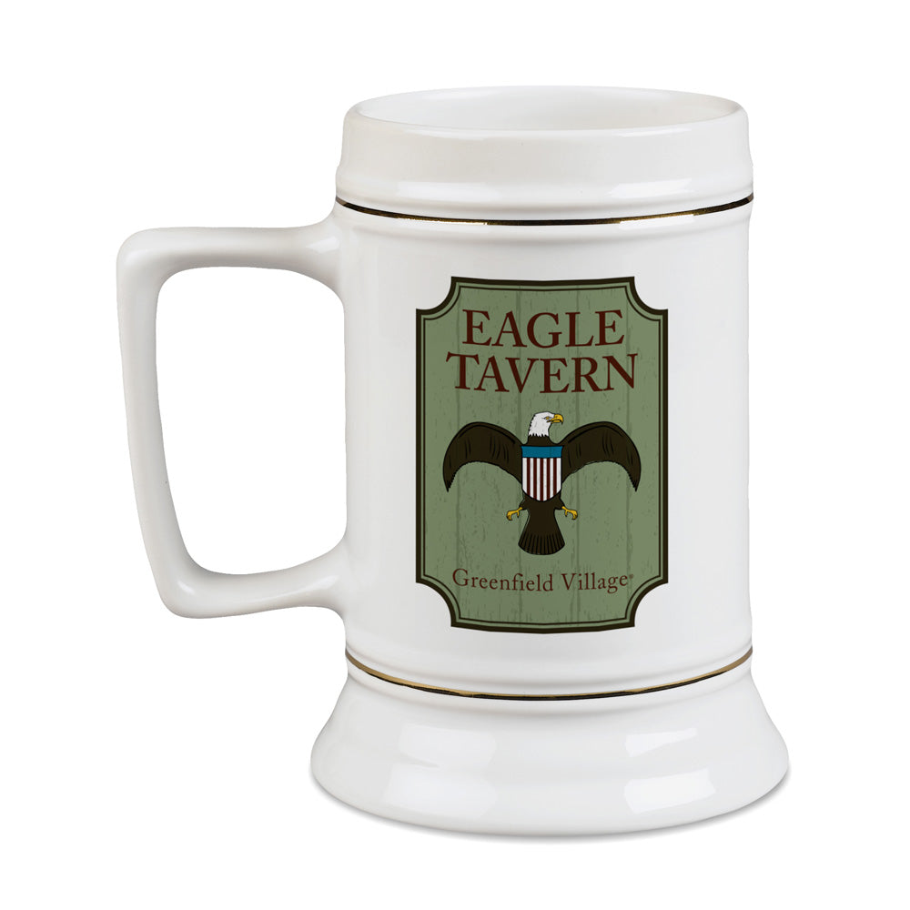 Introducing the Greenfield Village Eagle Tavern Stein—a white ceramic beer stein with a sturdy handle. It features a distinctive label that reads “Eagle Tavern, Greenfield Village” along with an illustrated eagle bearing a shield on its chest. Capturing the historic charm of 19th-century America, this collectible is ideal for history enthusiasts and devoted fans of Greenfield Village.