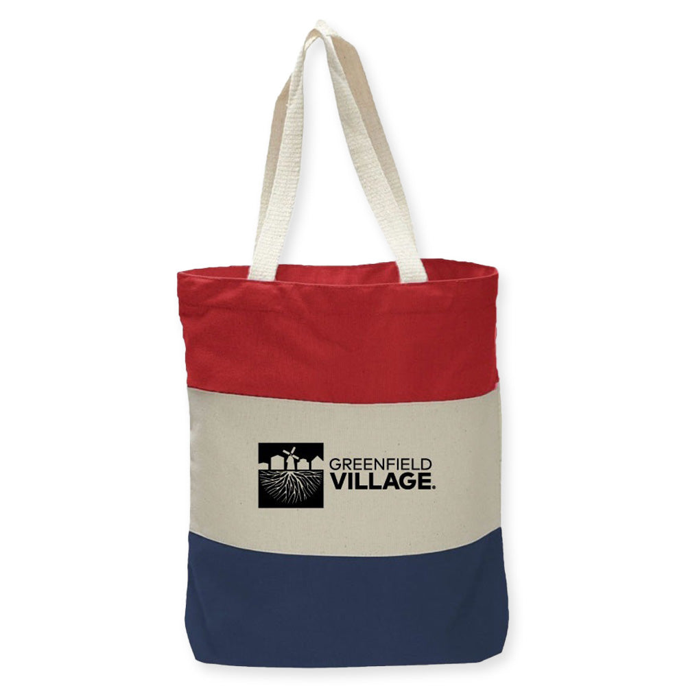 The Greenfield Village USA Colorblock Tote features red, beige, and blue panels. The beige side shows a black Greenfield Village logo with field, sun, and buildings. Includes two white handles—perfect for the USA 250th anniversary or museum visits.