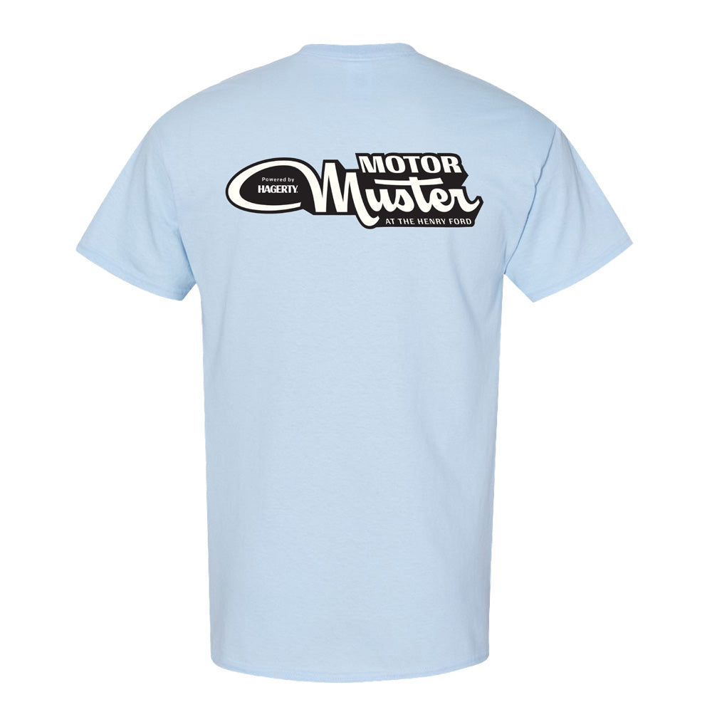 The Greenfield Village 2026 Motor Muster T-Shirt is light blue with a large black-and-white event logo on the upper back, plus "Presented by Hagerty" and "AT THE HENRY FORD" in smaller text.