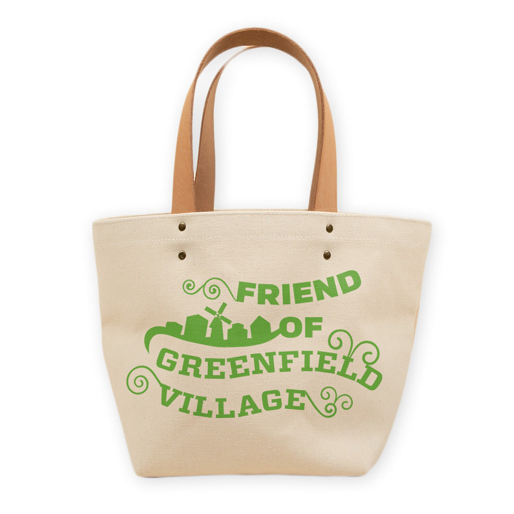 The Friend of Greenfield Village Tote is beige with brown handles and a green "FRIEND OF GREENFIELD VILLAGE" graphic with building and windmill silhouettes—a charming, historical-inspired accessory for everyday use.