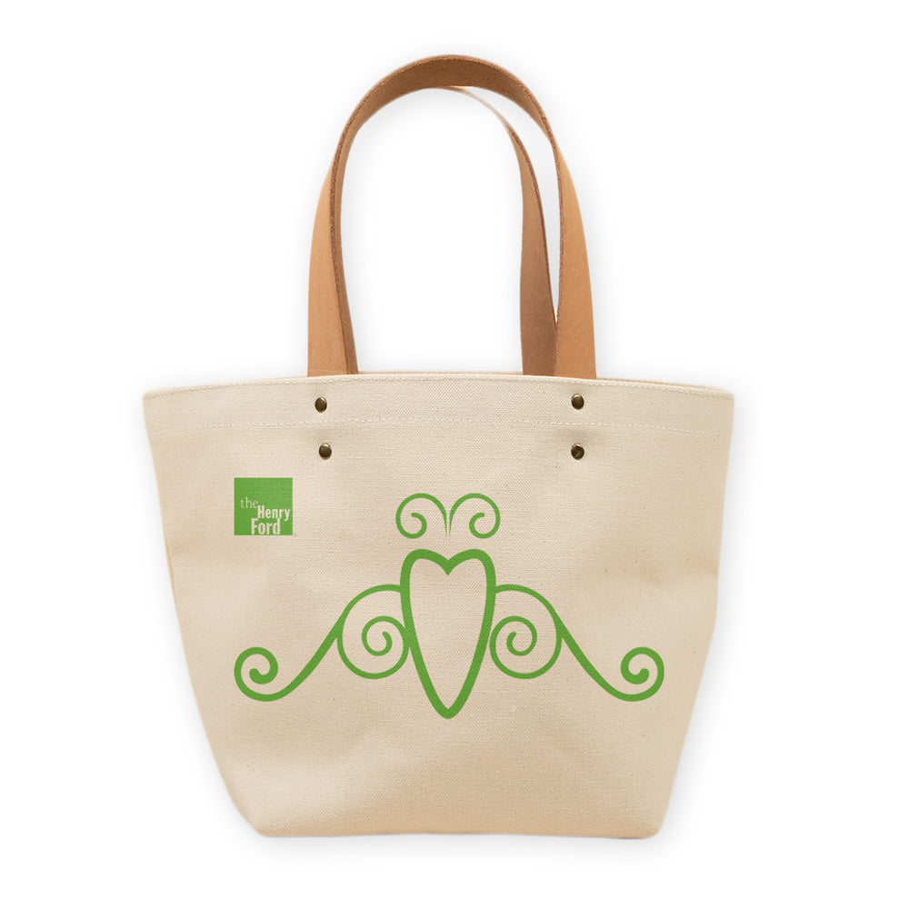 The Friend of Greenfield Village Tote is a beige canvas bag with tan leather handles, green decorative accents, and The Henry Ford logo—an ideal accessory for everyday use with a touch of history.