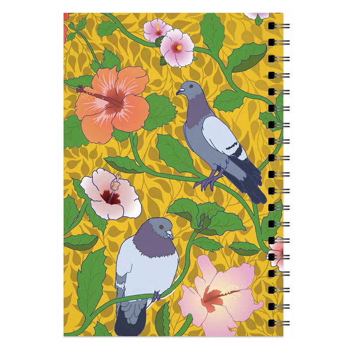 The Roberto Lugo Pigeon Art Journal is spiral-bound, featuring two pigeons amid green leaves and pink hibiscus flowers on a yellow patterned cover.