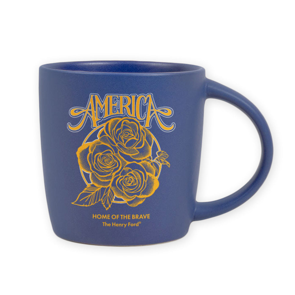 The Henry Ford® 1776 Concert Series Mug: a blue ceramic mug with yellow rose illustrations, "America" above "Home of the Brave," and The Henry Ford beneath—perfect for Greenfield Village fans and mug collectors.