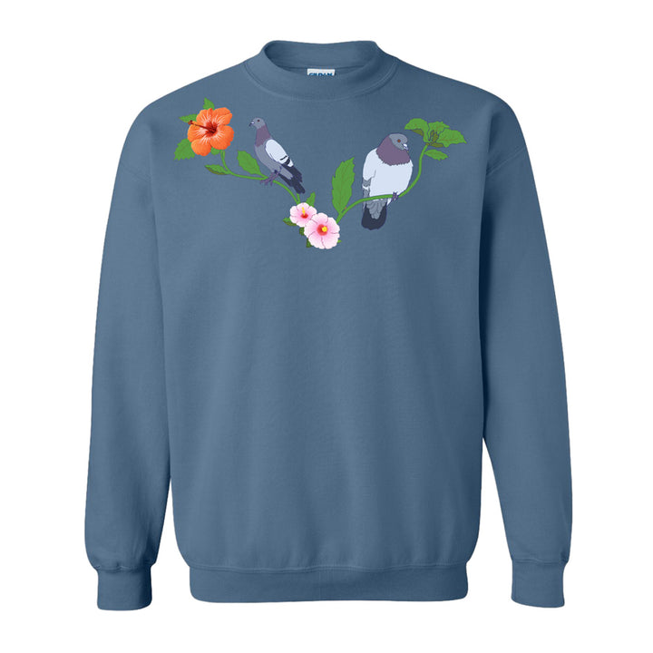 The Roberto Lugo Pigeon Crew Sweatshirt showcases two pigeons on leafy branches amid pink and orange flowers—a bold blue piece perfect for art lovers seeking standout street style.