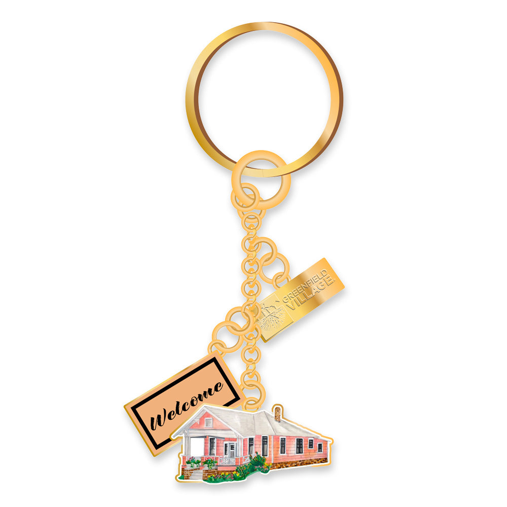 The Greenfield Village Jackson Home Dangle Keychain features a gold keyring with a pink house charm, Welcome tag, and Greenfield Village souvenir tag—an ideal keepsake for any collection.