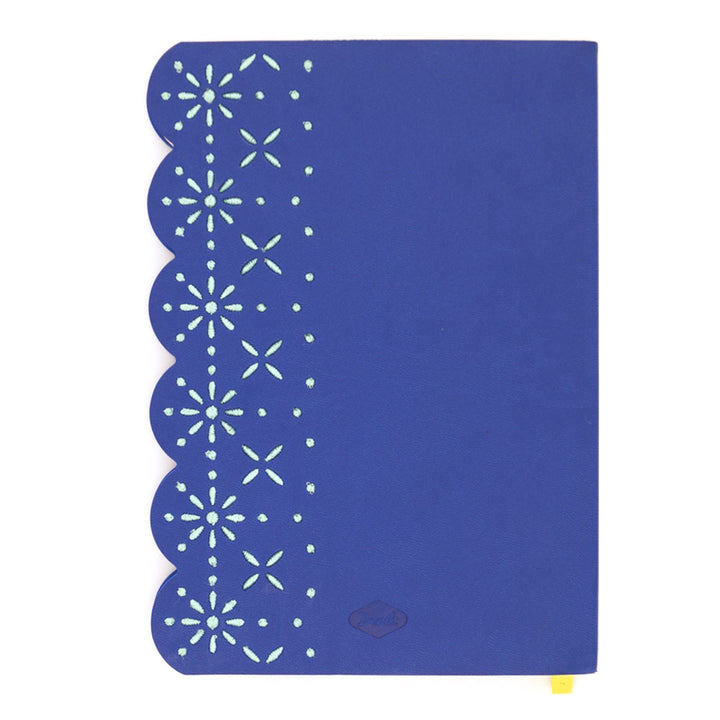 The Eyelet Embroidered Journal features blue vegan leather, a scalloped left edge with eyelet embroidery, light green stars and dots, and a small yellow ribbon bookmark for a charming touch.