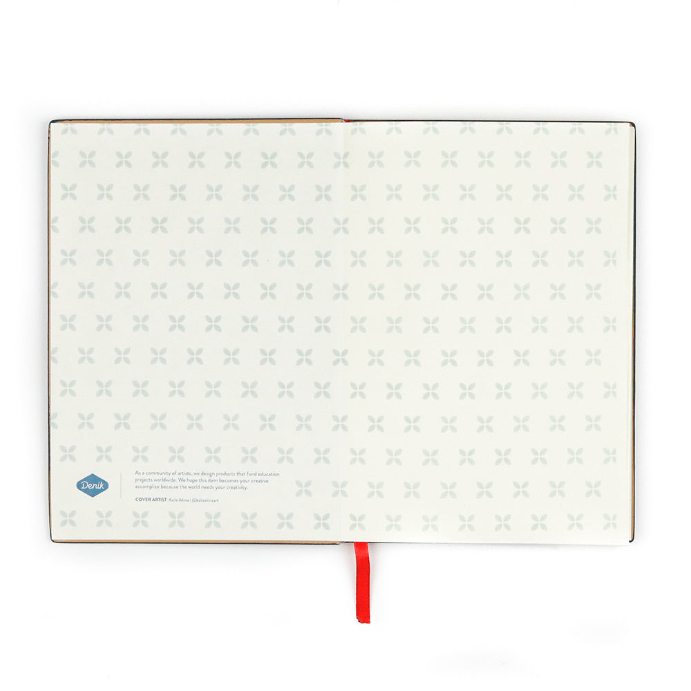 The Evelyn Blue Embroidered Journal features vegan leather covers, pages with a subtle gray X pattern, a small logo and text at the bottom left, and a red ribbon bookmark extending from the spine.