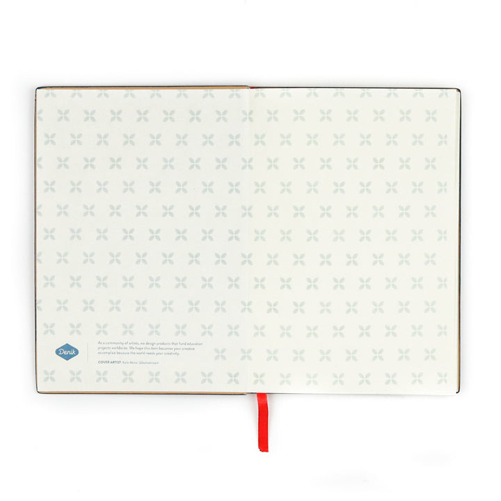 The Evelyn Blue Embroidered Journal features vegan leather covers, pages with a subtle gray X pattern, a small logo and text at the bottom left, and a red ribbon bookmark extending from the spine.