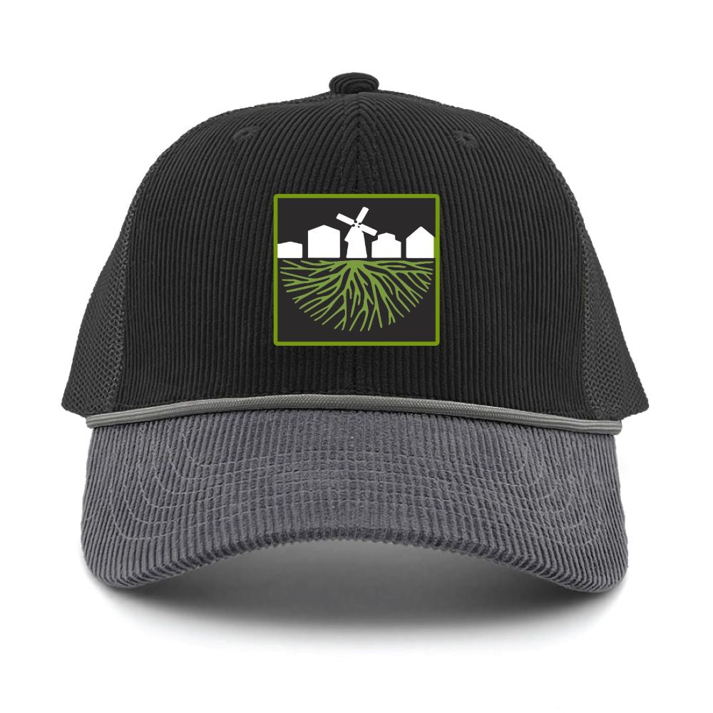 The Greenfield Village Corduroy Trucker Cap features a black and gray mesh design with a front patch depicting white houses, a windmill, and green roots—a tribute to the picturesque landscape of Greenfield Village, the renowned living history museum.