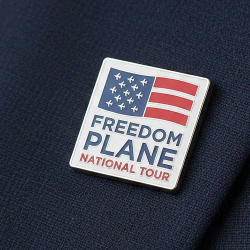 The Freedom Plane Tour Lapel Pin showcases a stylized American flag with airplane icons as stars and “FREEDOM PLANE NATIONAL TOUR” text on dark fabric, honoring American heritage.