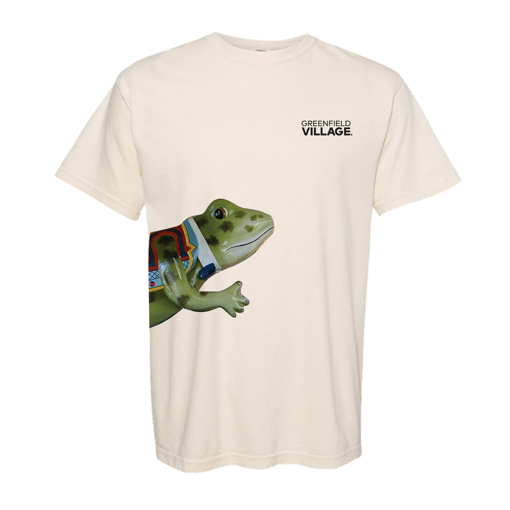 Introducing the Hershel the Frog T-Shirt: a beige tee with “Greenfield VILLAGE.” printed on the left chest and a vibrant, oversized Hershel the Frog graphic playfully stretching from the lower left side—a tribute to Greenfield Village’s whimsical spirit and its cherished Herschell-Spillman carousel.