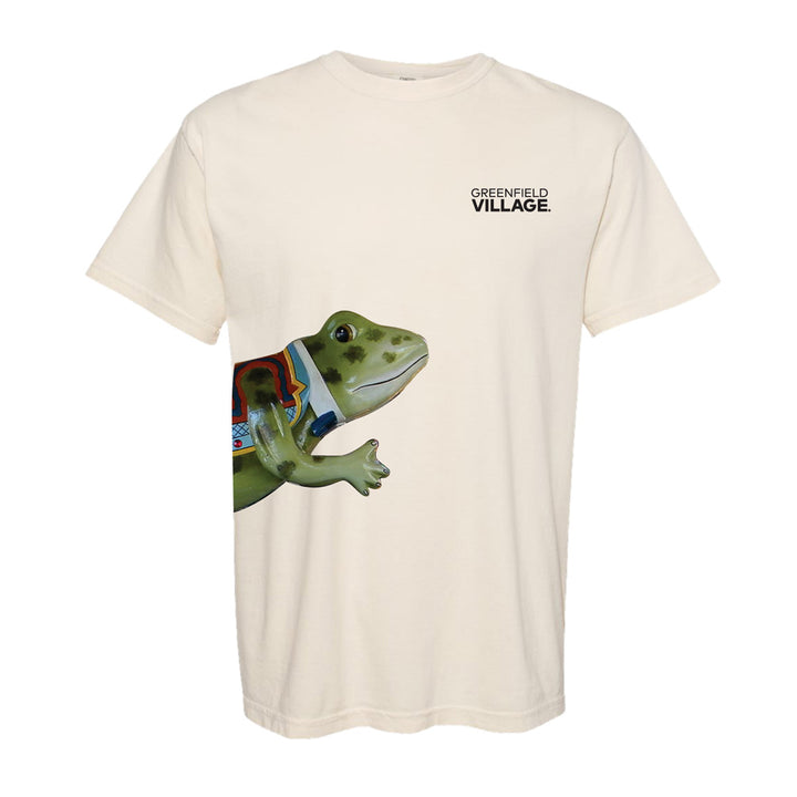 Introducing the Hershel the Frog T-Shirt: a beige tee with “Greenfield VILLAGE.” printed on the left chest and a vibrant, oversized Hershel the Frog graphic playfully stretching from the lower left side—a tribute to Greenfield Village’s whimsical spirit and its cherished Herschell-Spillman carousel.