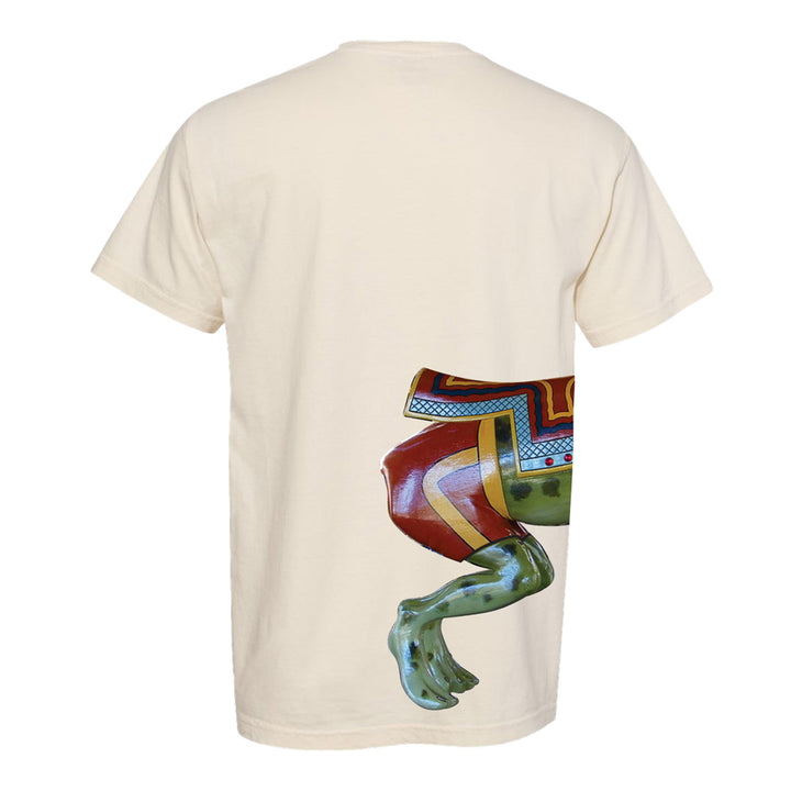 The Hershel the Frog T-Shirt is a cream-colored shirt featuring a vibrant, patterned frog’s back half—including green legs and a multicolored saddle-inspired design—printed on the lower right side of the back. The whimsical artwork draws inspiration from the Herschell-Spillman carousel at Greenfield Village.