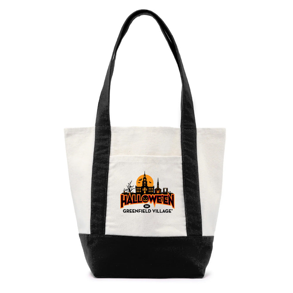 The Henry Ford® Greenfield Village Halloween Tote is a white and black bag with long handles, crafted from recycled cotton canvas. The front displays an orange Halloween-themed logo featuring haunted house silhouettes and the text “Halloween Greenfield Village,” making it the perfect stylish accessory for fans of the living history museum to celebrate the season.