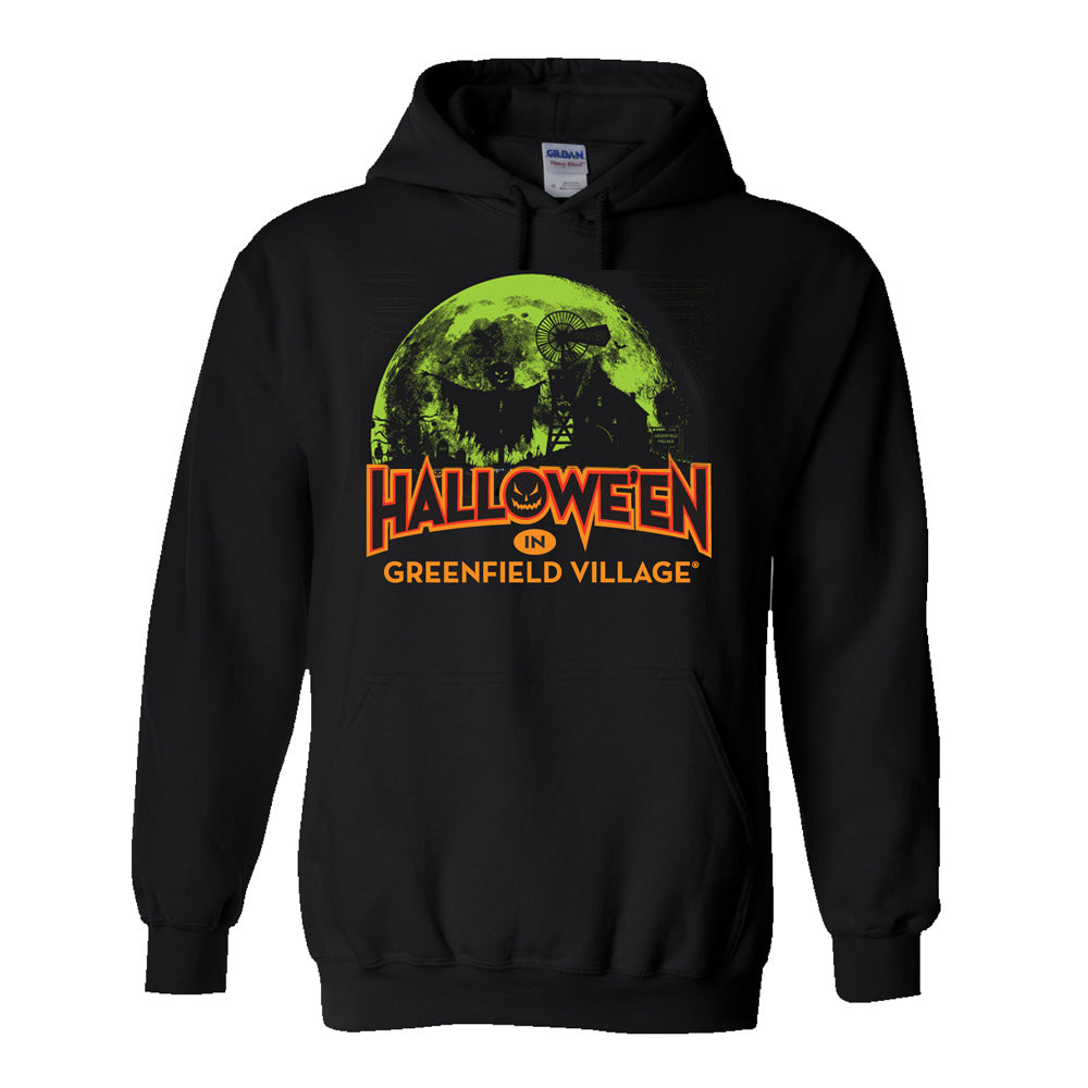 The Henry Ford® Greenfield Village Halloween Glow Hooded Sweatshirt features a black design with a green full moon, witch, and tree graphic. Bold orange text underneath the image reads “Halloween in Greenfield Village,” making it a spooky and stylish pick for fans of Greenfield Village.