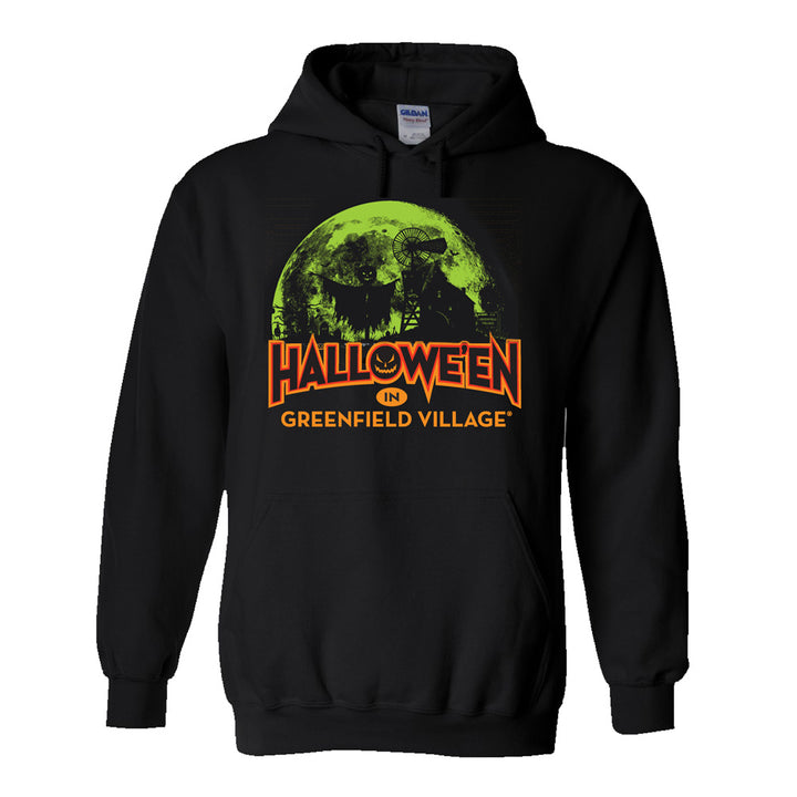 The Henry Ford® Greenfield Village Halloween Glow Hooded Sweatshirt features a black design with a green full moon, witch, and tree graphic. Bold orange text underneath the image reads “Halloween in Greenfield Village,” making it a spooky and stylish pick for fans of Greenfield Village.