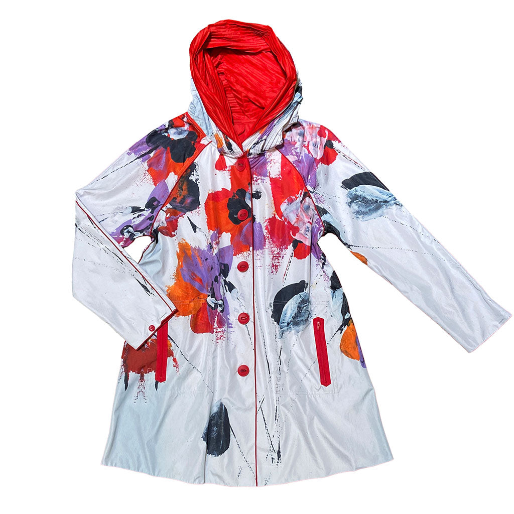 The Splash Women's Jacket is a hooded, knee-length coat with a women's fit, featuring a white base with bold abstract floral patterns in red, orange, purple, and black. It has red buttons, pockets, and a red-lined hood.