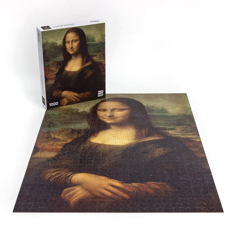 A completed Leonardo Da Vinci - Mona Lisa Puzzle with 1000 pieces is displayed on a white surface, with its box featuring the iconic artwork standing behind it.