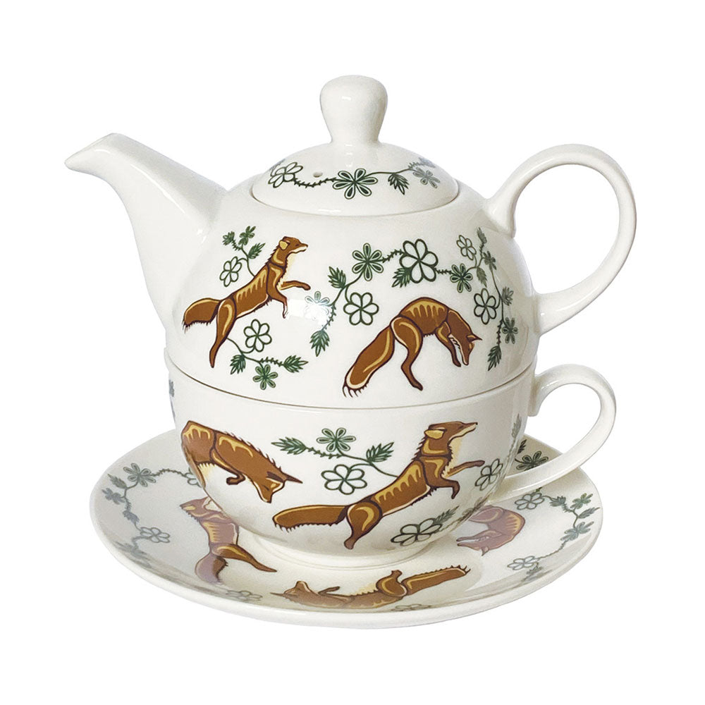 The Native Northwest Fox Tea Set features a white ceramic teapot stacked on a matching handled teacup and saucer, all decorated with brown foxes and green floral patterns inspired by Indigenous art.