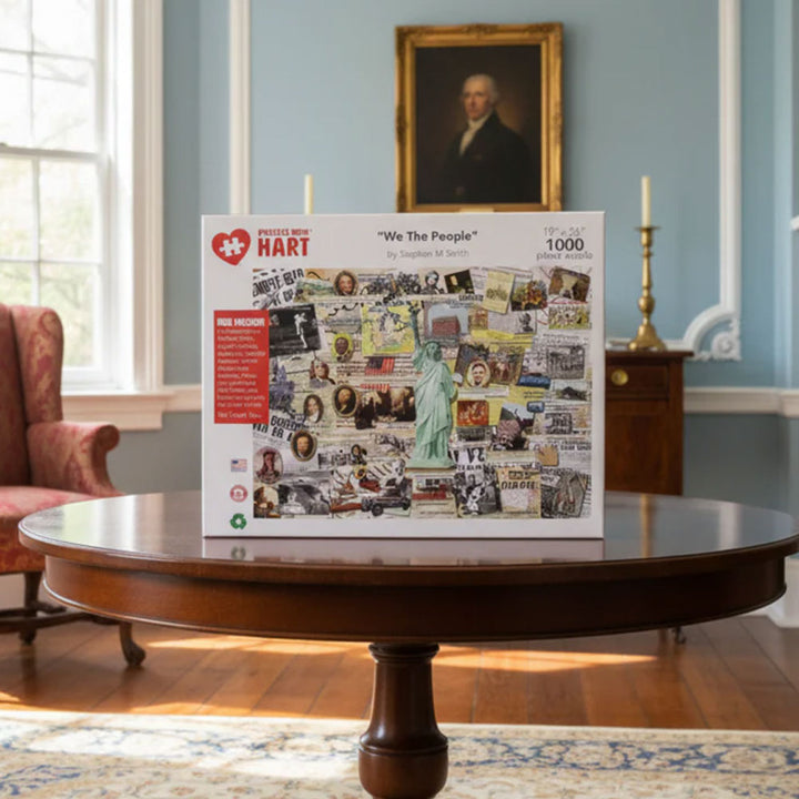 The We The People 1000pc Jigsaw Puzzle, featuring American historical images, is displayed on a round wooden table in a classic blue-walled room with a red armchair and portrait, creating an engaging educational experience.
