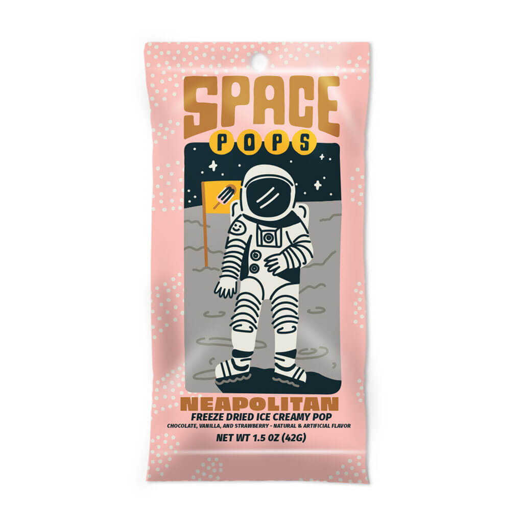 A pink package labeled “Space Pops Freeze Dried Neopolitan Ice Creamy Pops” showcases an illustrated astronaut holding a crunchy ice cream bar while standing on the moon, surrounded by stars and planets. This space-themed treat offers freeze-dried ice cream in chocolate, vanilla, and strawberry flavors.