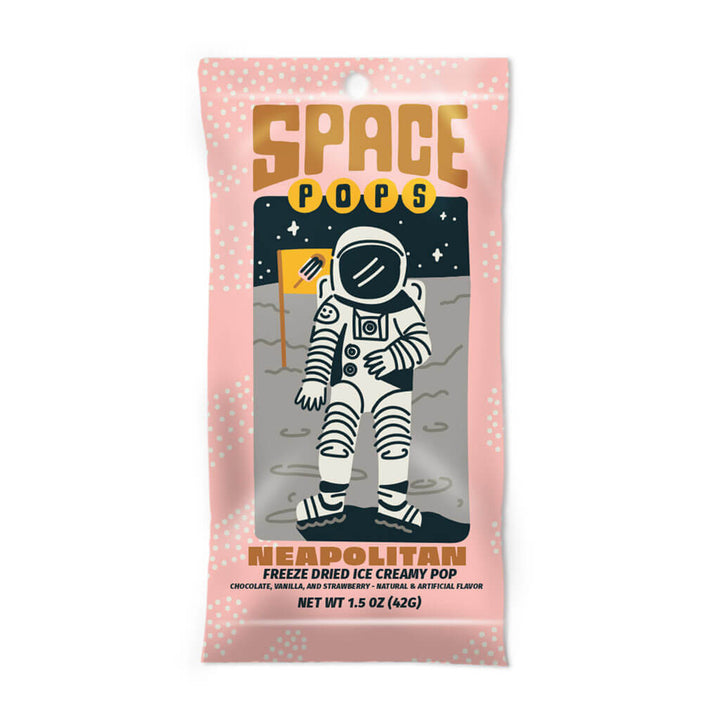 A pink package labeled “Space Pops Freeze Dried Neopolitan Ice Creamy Pops” showcases an illustrated astronaut holding a crunchy ice cream bar while standing on the moon, surrounded by stars and planets. This space-themed treat offers freeze-dried ice cream in chocolate, vanilla, and strawberry flavors.