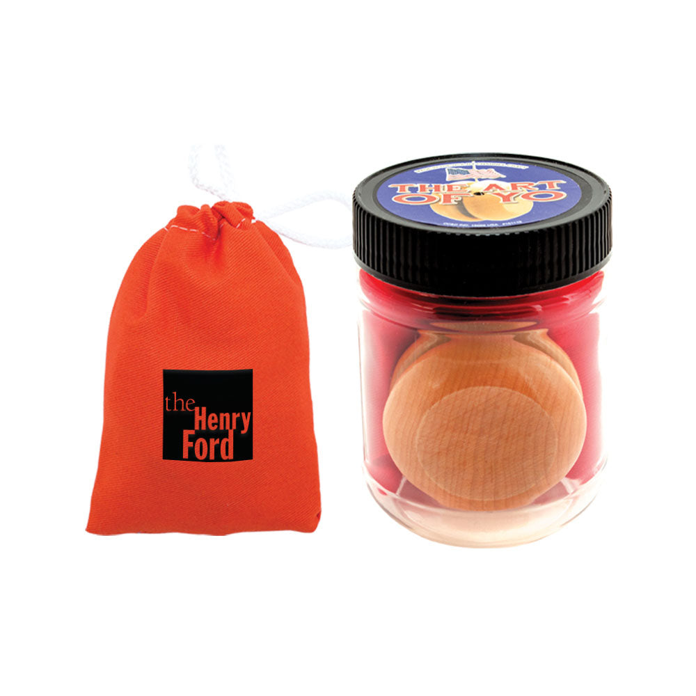 A small orange drawstring pouch labeled The Henry Ford sits beside a clear plastic jar with a black lid, holding the Classic Yo-Yo and red string—everything needed to practice and master impressive yo-yo tricks.