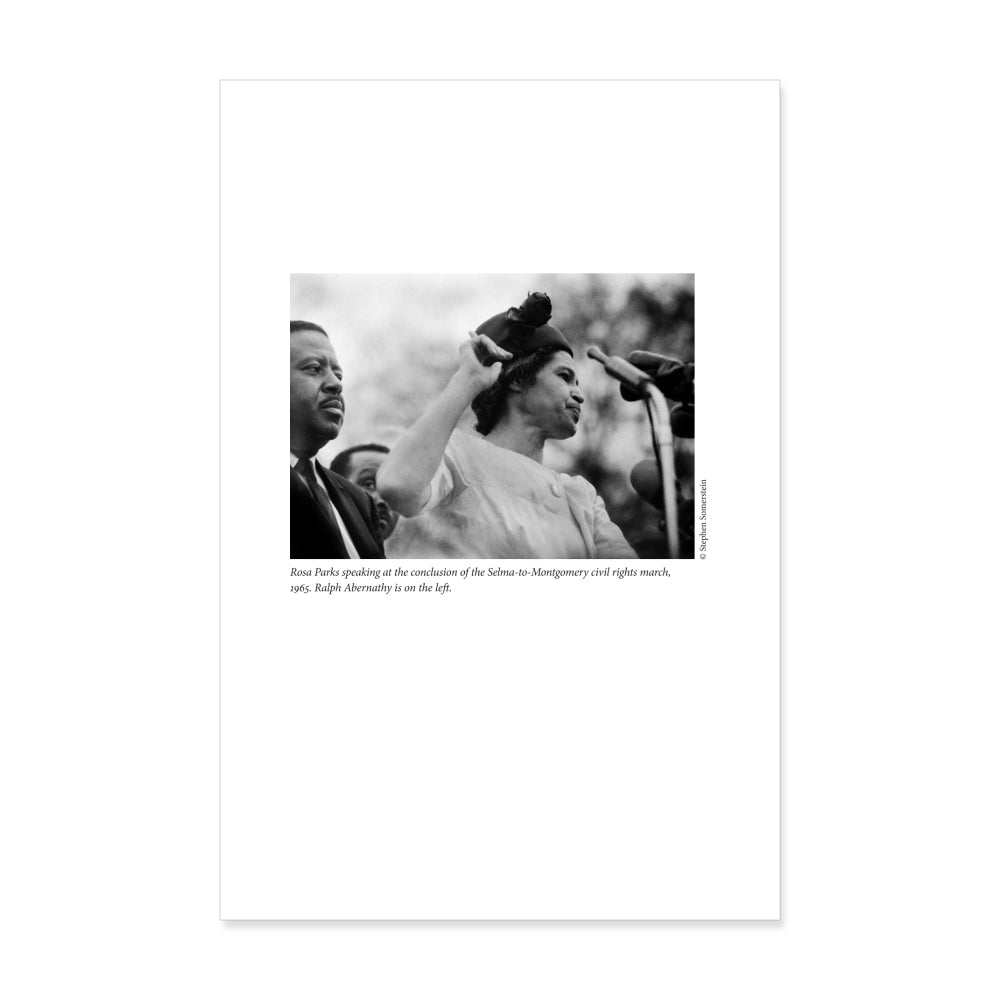 Black-and-white photo from "The Rebellious Life of Mrs. Rosa Parks" shows Rosa Parks at a microphone during the 1965 Selma-to-Montgomery march, with a man beside her—an iconic moment in civil rights history.
