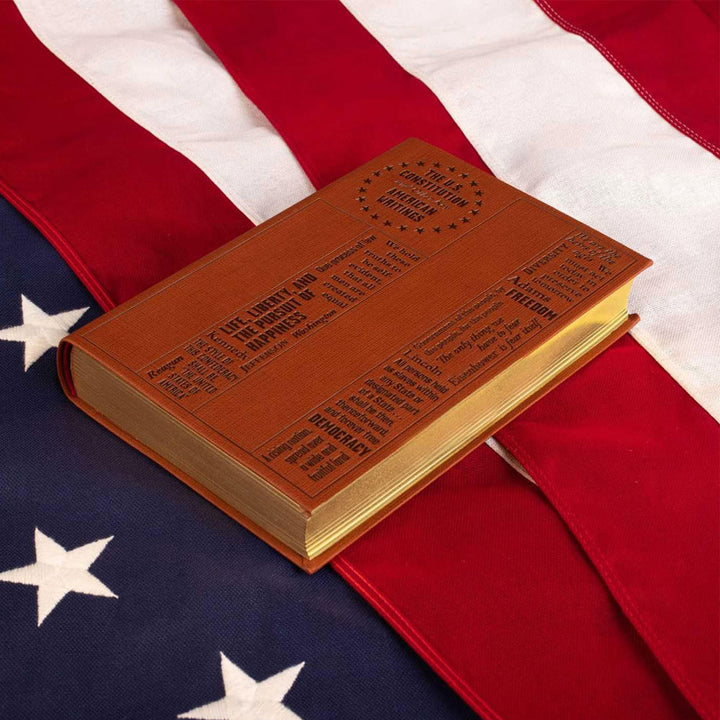 The U.S. Constitution and Other Key American Writings (Word Cloud Classics), a brown book with engraved text and a circular star design, rests on a folded American flag, representing the enduring legacy of America’s Founding Fathers.