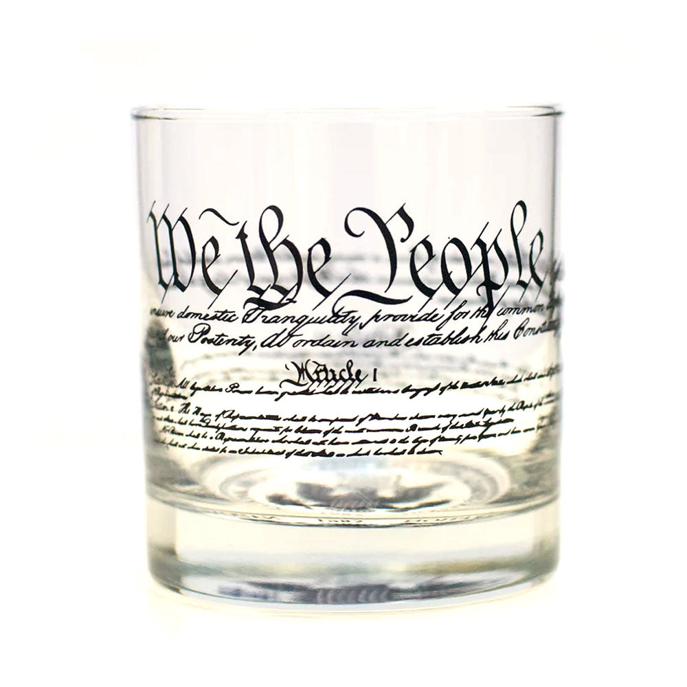 The Declaration of Independence Rocks Glass displays "We the People" and script from the document in black text wrapping around the glass. The empty glass is shown against a white background.