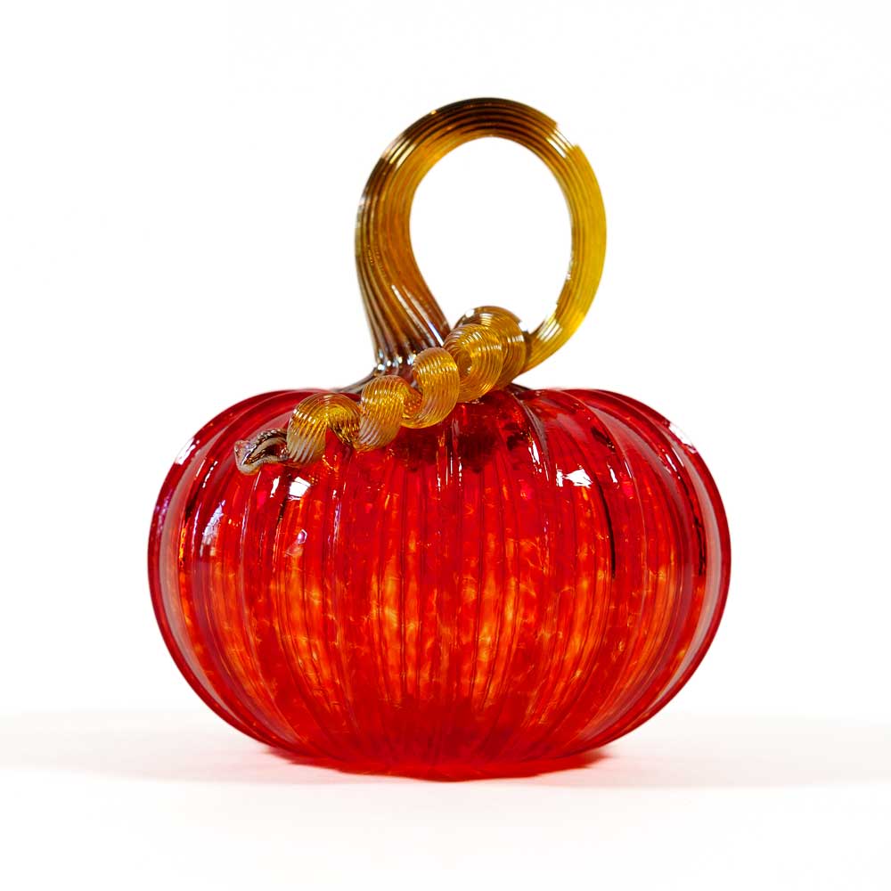 A beautiful collectible keepsake, the Small Glass Pumpkin - Cherry features a vibrant red hand-blown glass body with vertical ridges and a curled, translucent gold stem. Inspired by the artistry of Greenfield Village, this exquisite pumpkin is displayed on a white background.