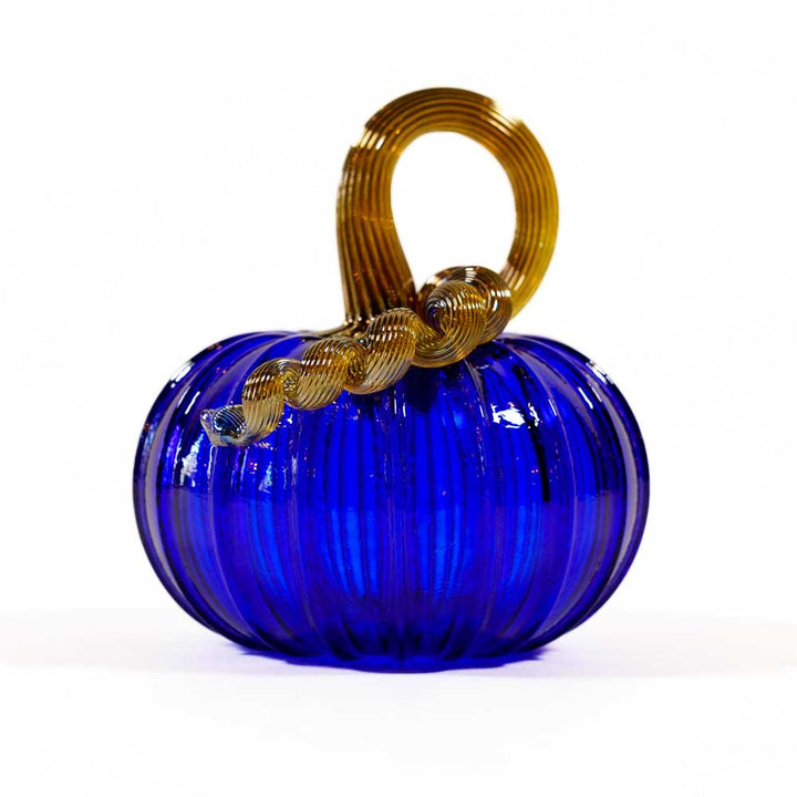 The Small Glass Pumpkin - Cobalt features hand blown blue glass with a ribbed surface and a curly golden-brown stem, displayed on a white background—a unique collectible keepsake pumpkin.