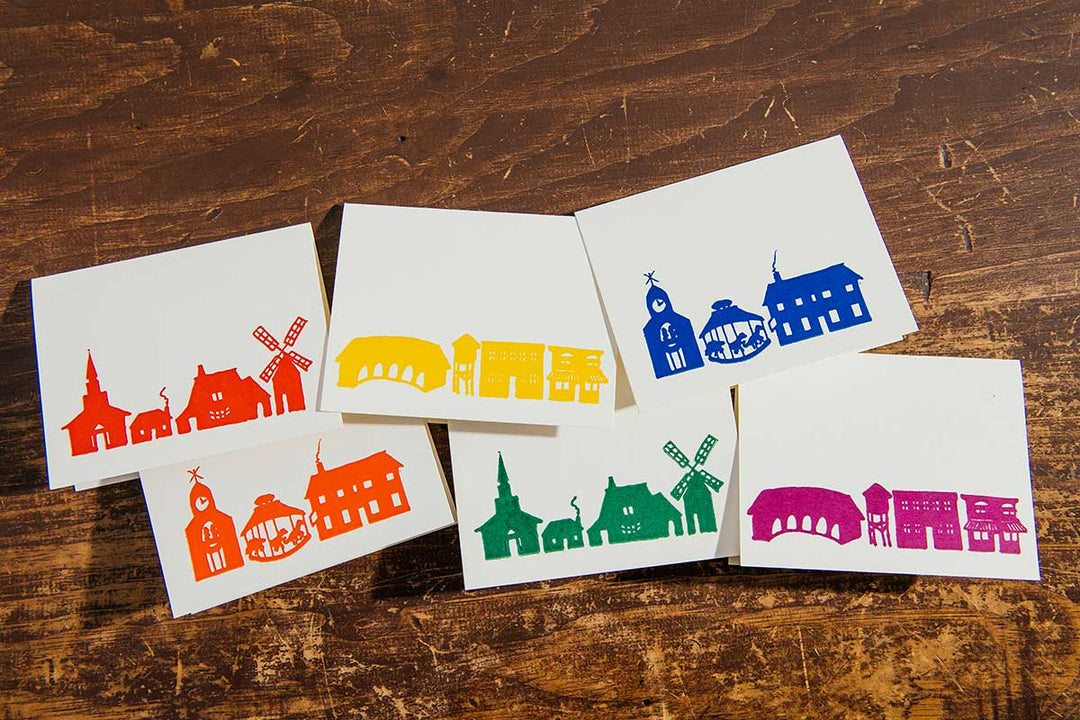 The Rainbow Village Card Set of 6 features white cards with colorful cityscape silhouettes of Greenfield Village, each uniquely designed and printed using photopolymer plates on an 1880s treadle press.