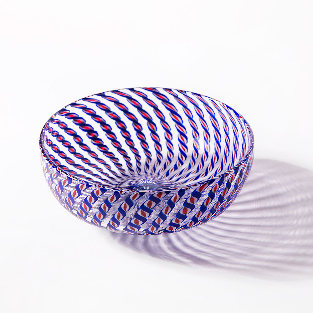 The 2026 Candy Cane Bowl, expertly crafted by glassblowers, features blue, red, and white twisted stripes and casts a striking patterned shadow on a white surface.