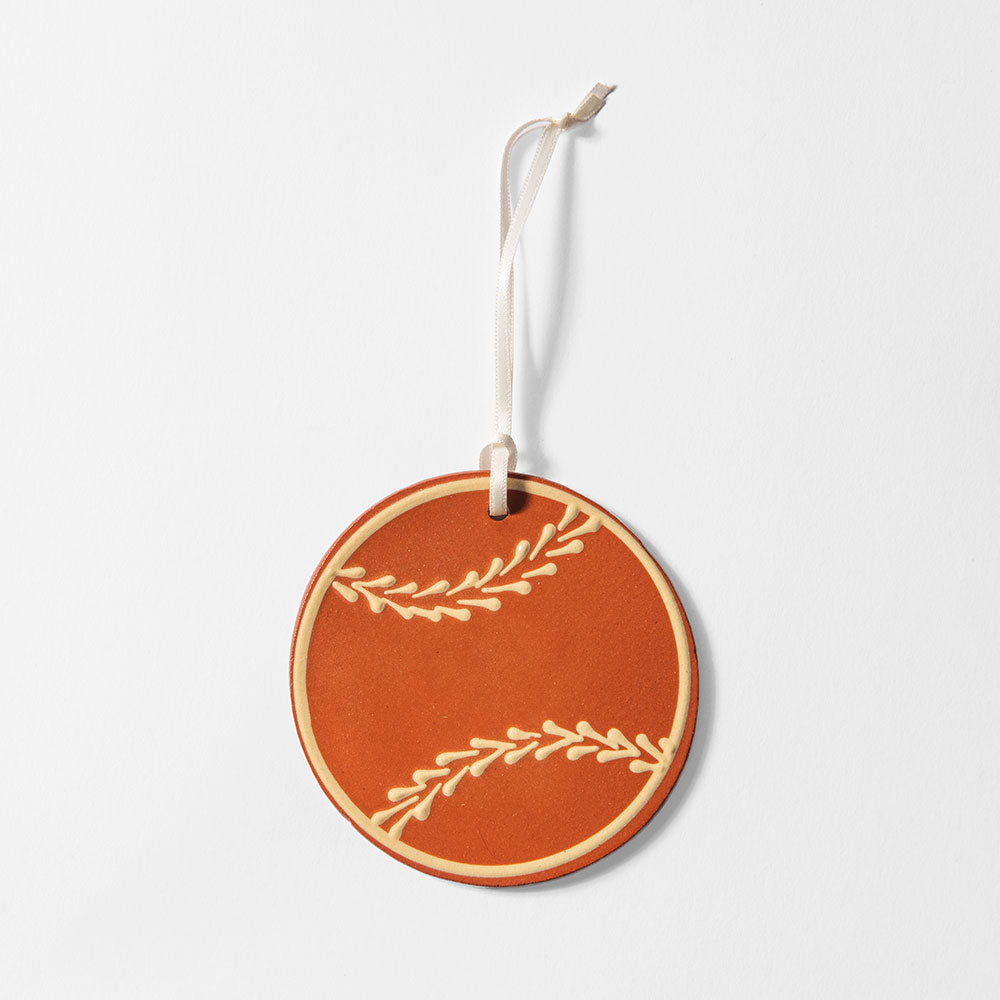 The Base Ball Redware Ornament is a round, terracotta-toned handcrafted ornament made from redware clay with a simple leaf design, hanging from a cream ribbon against a white background.
