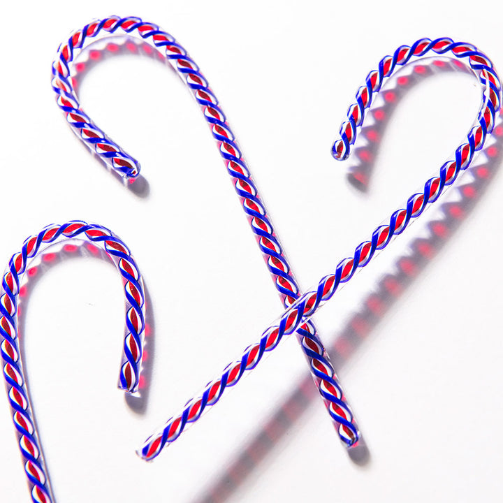 Three 2026 Candy Cane limited-edition treats with twisted red, white, and blue stripes rest on a white surface, casting soft shadows—a festive tribute to America’s 250th anniversary.