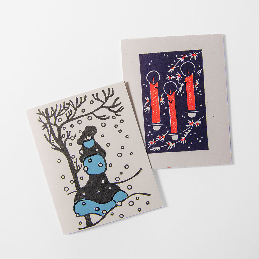 The 2026 Candy Cane Card Set includes two handprinted cards: one with a blue snowman under snowy branches, the other with three red candles, holly, and stars on a dark backdrop—perfect for adding holiday charm.